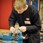 A focused man crafting metal in a workshop with precision tools and equipment.