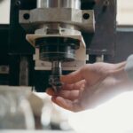 Detailed shot of a CNC machine spindle being adjusted by a human hand in a workshop setting.