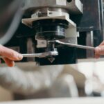 Close-up of hands adjusting a CNC machine using wrenches in an industrial setting.